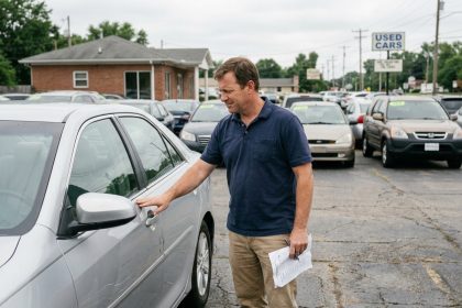 Homme examinant une voiture familiale d'occasion dans un parking de concessionnaire automobile