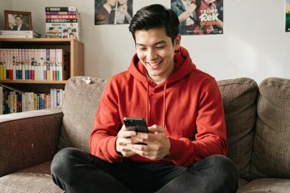 Jeune homme lisant le scan One Piece sur smartphone dans son salon entouré de mangas